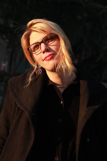 A photo of a blonde trans femme, Zefyr Lisowski, wearing glasses and a heavy winter coat. She's squinting and smiling, slightly.